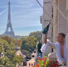 a woman standing on top of a balcony next to a building with the eiffel tower in the background