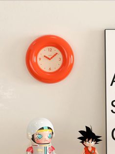 an orange clock on the wall next to a small figurine and a sign