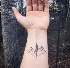 a person's hand with a small tattoo on the wrist and mountains in the background