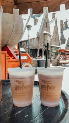 two plastic cups sitting on top of a table with straws in each cup and hog potter's village behind them