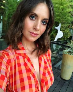 a woman in an orange and pink shirt posing for the camera with her hand on her hip