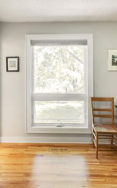 an empty room with a chair, window and pictures hanging on the wall in front of it