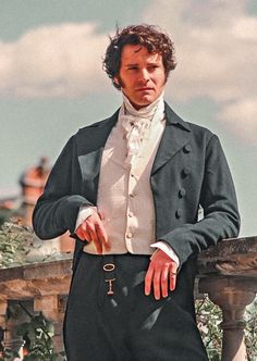 a man in a suit and tie standing next to a fence with his hands on his hips