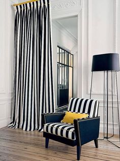 a black and white striped chair sitting in front of a window next to a lamp