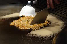 a person scooping corn out of a frying pan with a spatula on it