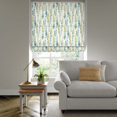 a white couch sitting under a window next to a table with a lamp on it