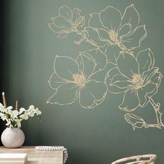 a vase with flowers sitting on top of a wooden table next to a green wall