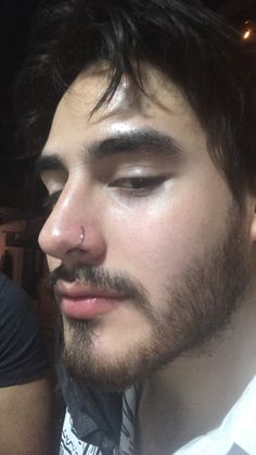 a close up of a person wearing a tie and piercing on his nose with other people in the background