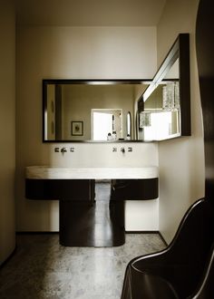 a modern bathroom with two sinks and large mirrors on the wall, along with a black chair