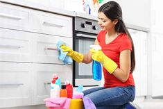 a woman in red shirt and yellow gloves cleaning oven with sponges on the counter