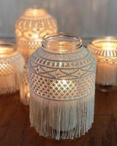 some white candles are sitting on a table with tassels around the candle holders