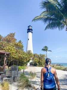 a woman walking down a path towards a light house with palm trees in the foreground