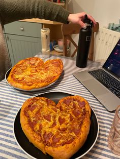 two heart shaped pizzas sitting on plates in front of a laptop