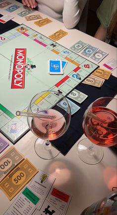 a monopoly board game with two glasses of wine on the table next to each other