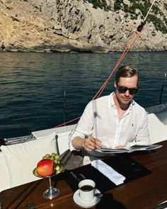 a man sitting at a table on top of a boat in the ocean reading a book