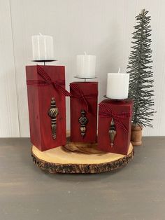 three candles are wrapped in red paper and placed on a wood slice with a christmas tree