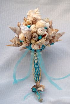 a bridal bouquet with seashells and blue ribbons on a white cloth background