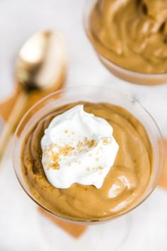 two desserts with whipped cream on top and spoon in the middle, sitting on a table