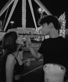 a man and woman eating food in front of a ferris wheel at an amusement park