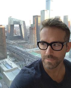 a man wearing glasses looking at the camera in front of a cityscape with skyscrapers