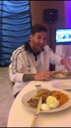 a man sitting at a table with plates of food in front of him and smiling