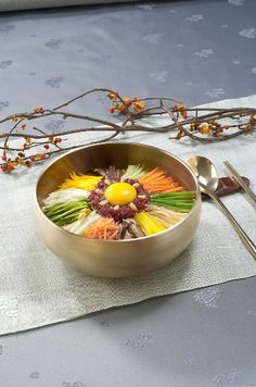 a metal bowl filled with food on top of a table next to utensils