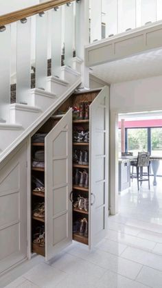 an open shoe cabinet under the stairs in a room with white walls and flooring