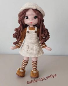 a crocheted doll with brown hair wearing a white dress and hat, standing on a table