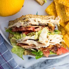 a sandwich with lettuce, tomato, and meat on it next to tortilla chips