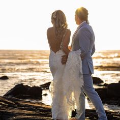 a bride and groom standing on the rocks by the ocean at sunset or sunrise time