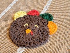 a crocheted turkey hat laying on top of a brown tablecloth covered floor