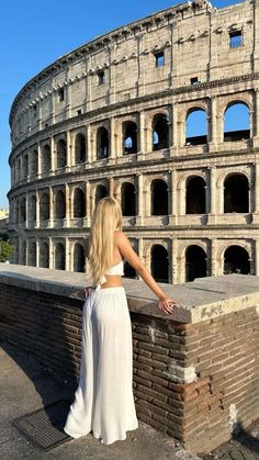 a woman is standing in front of an old roman colossion with her hand on the wall