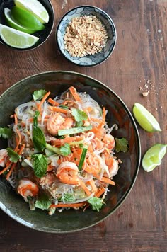 a bowl filled with shrimp and vegetables on top of a wooden table next to lime wedges