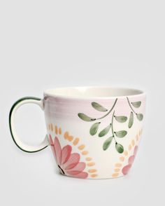 a white cup with pink flowers and green leaves on the inside is sitting in front of a gray background