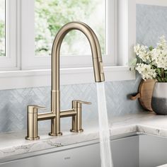 a kitchen faucet with water running from it's spout in front of a window