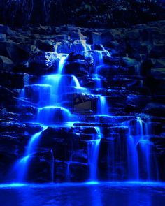 a waterfall lit up with blue lights in the night sky and water flowing down it