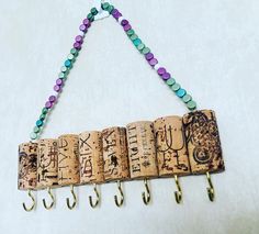 a row of wine corks hanging from hooks on a white wall with beads and charms attached to them