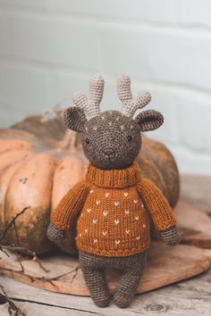 a knitted giraffe wearing an orange sweater and standing next to pumpkins