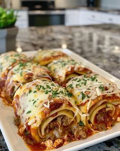 a white plate topped with lasagna rolls covered in cheese and sauce on top of a marble counter