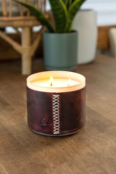 a candle sitting on top of a wooden table next to a potted plant