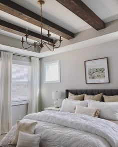 a white bed sitting under a chandelier in a bedroom next to a window