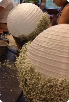 two paper lanterns are sitting on a table with flowers in them and people standing around