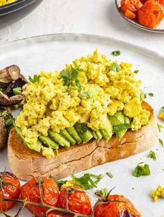 an open face sandwich topped with scrambled eggs and tomatoes on a plate next to mushrooms