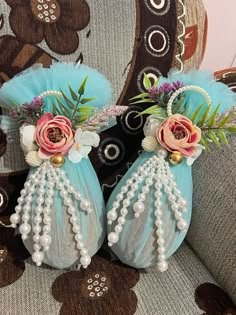 two blue vases with flowers and pearls are sitting on a patterned fabric chair cushion