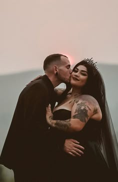 a man and woman kissing each other in front of the sun with tattoos on their arms