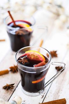 two glasses filled with mulled wine on top of a wooden table next to cinnamon sticks