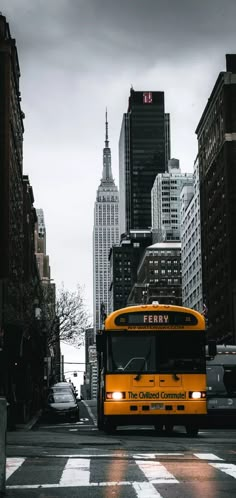 a yellow bus is driving down the street in front of tall buildings and skyscrapers