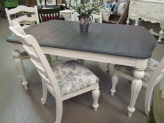 a table and chairs in a store with flowers on the top one chair is upholstered