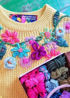 an open box filled with yarn and crochet flowers on top of a wooden table