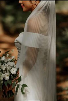 a woman in a white dress holding a bouquet and looking off into the distance with her back to the camera